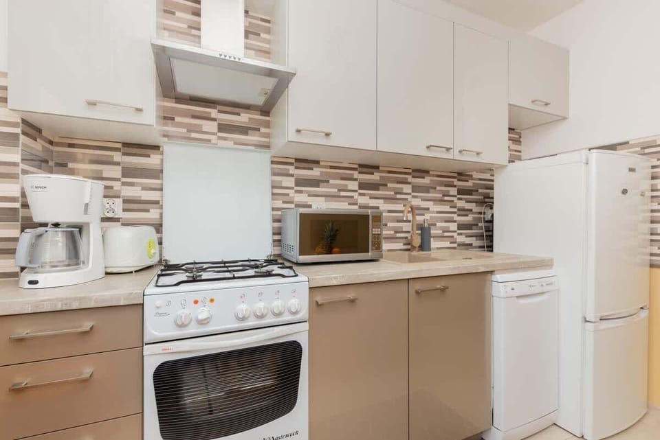 A functional kitchen space with a tiled backsplash, white appliances, and wooden accents.

