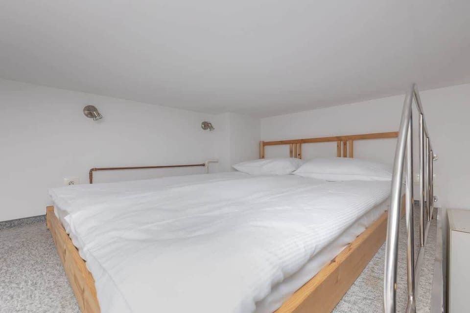 A lofted sleeping space with a white bed and a wooden rail, creating a cozy private nook.

