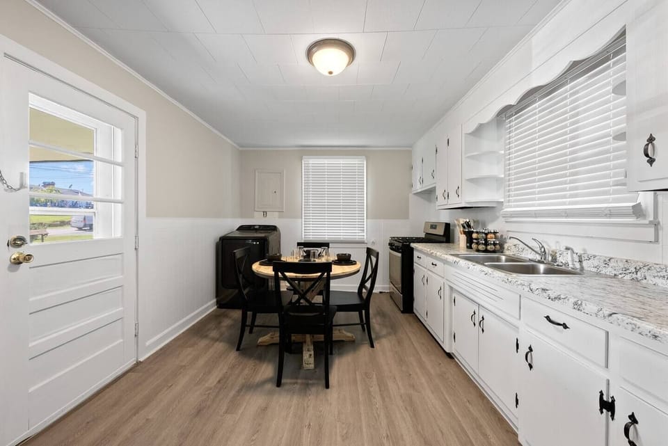 The kitchen is equipped with stainless steel appliances, including a refrigerator and a stove, which add a sleek, modern touch. A window with blinds on one wall allows natural light to illuminate the room, complemented by a ceiling light fixture above.
