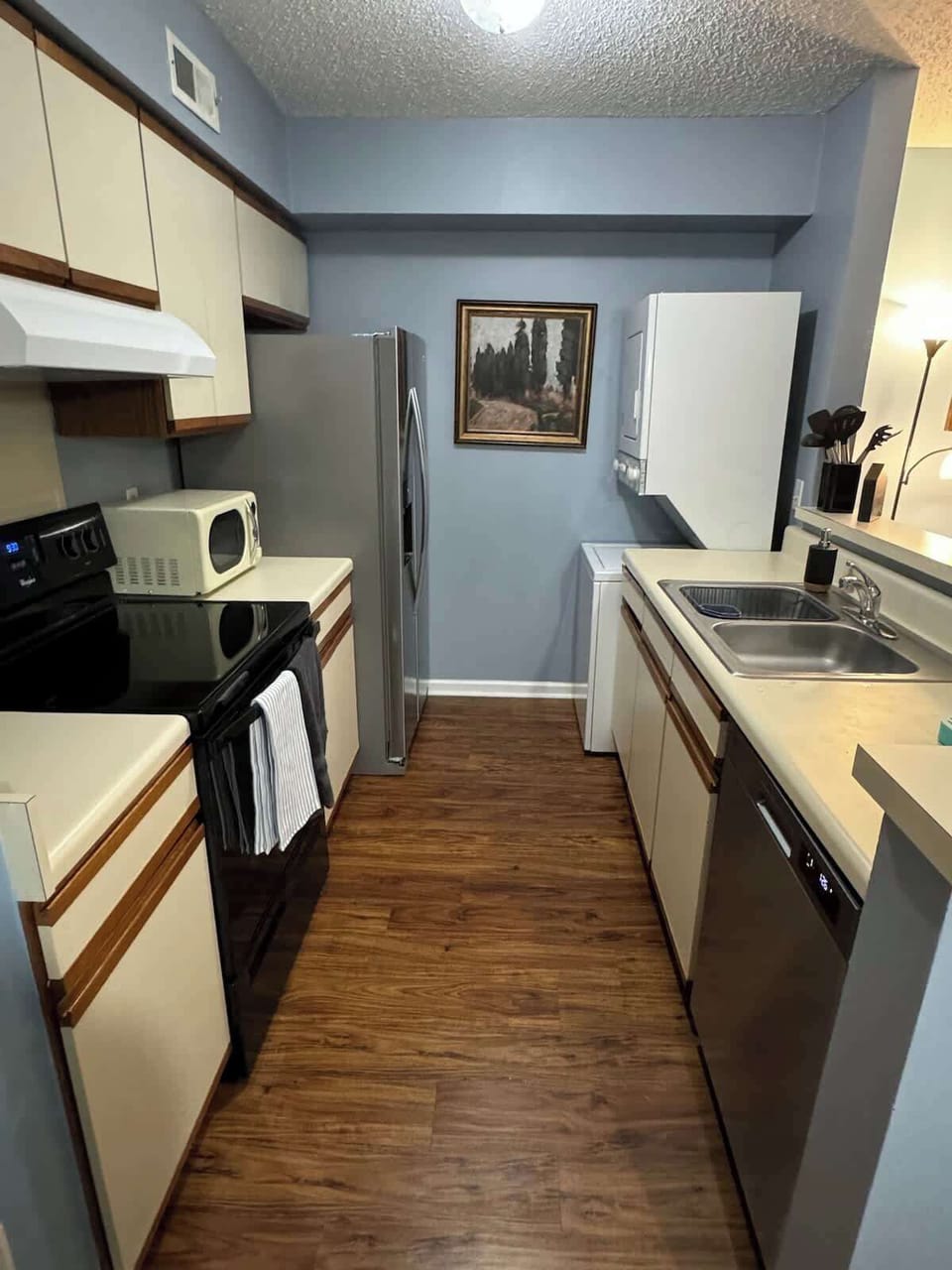 Kitchen with large refrigerator and freezer, sink, stovetop, oven, microwave, dishwasher, in-unit washer and dryer, and storage for provided kitchenware
