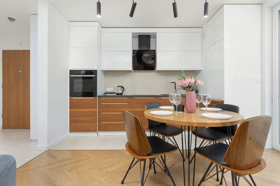 An open-plan kitchen and dining area featuring a mix of light wood tones and dark accents, illuminated by natural light through large windows.