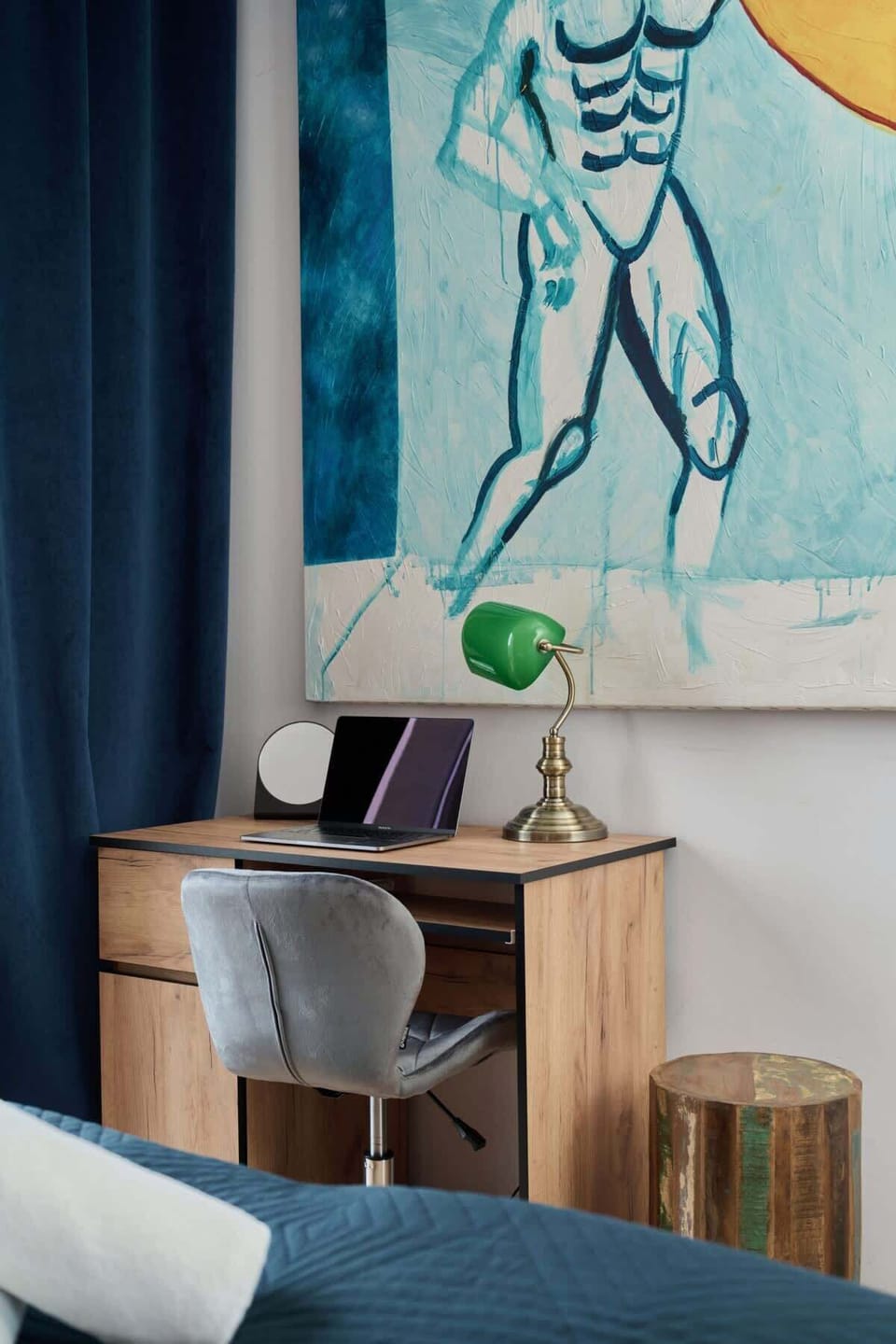 A bright bedroom with large windows, colorful wall art, and a comfortable double bed with blue accents.

