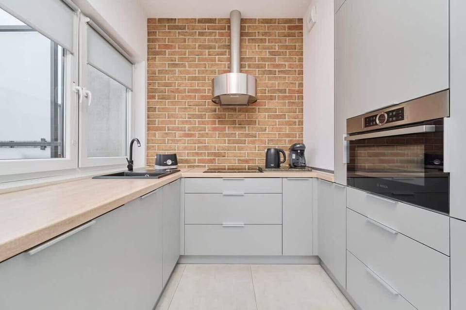 A sleek kitchen with white cabinets, a brick backsplash, and a wide window providing ample light.

