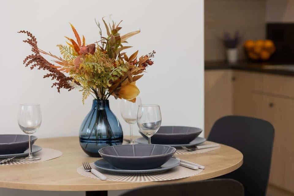 A dining table set for two with elegant dishes and a vase of flowers as a centerpiece.
