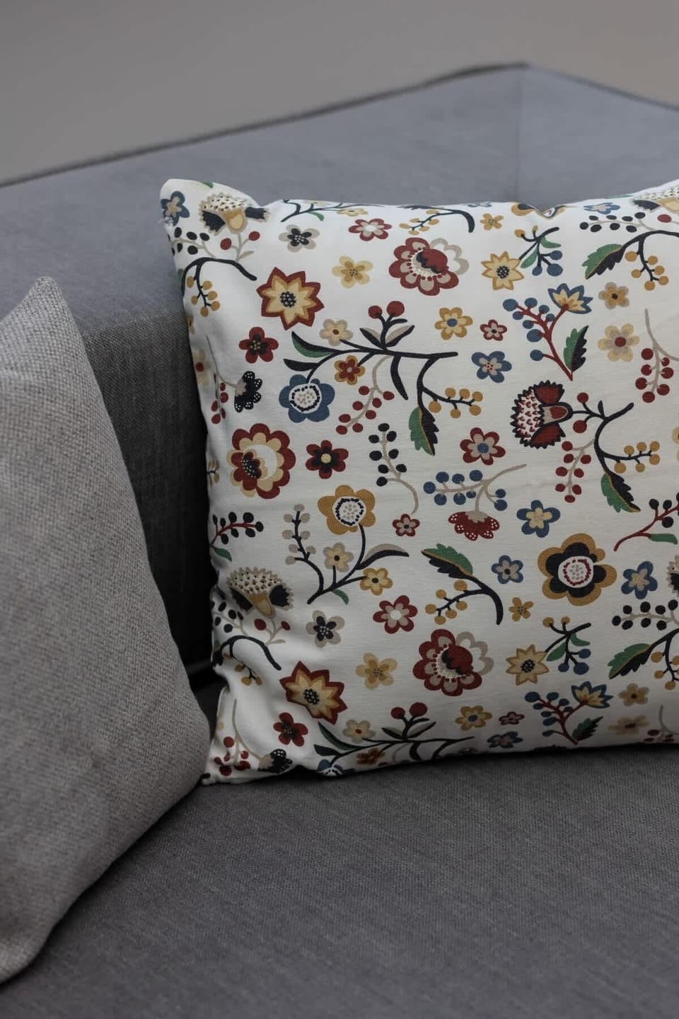 A close-up of a decorative pillow with a floral pattern on the gray sofa.
