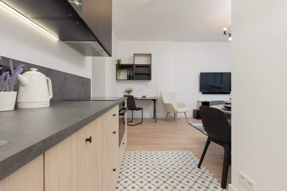 A partial view of the kitchen, showing the countertop, backsplash, and seating in the background.
