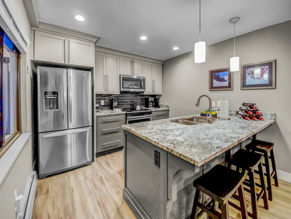 Modern kitchen with stainless-steel appliances, granite countertops, and a spacious island with seating. Fully equipped for cooking and après-ski meals during your Park City stay. Bright lighting and stylish finishes create a welcoming, functional space.