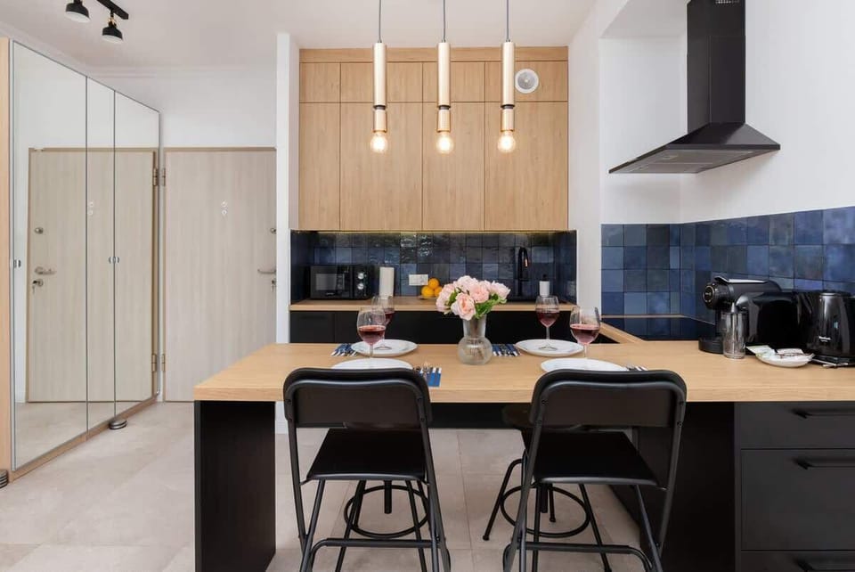 A fully equipped kitchen with black dining chairs, hanging lights, and ample cabinet space.