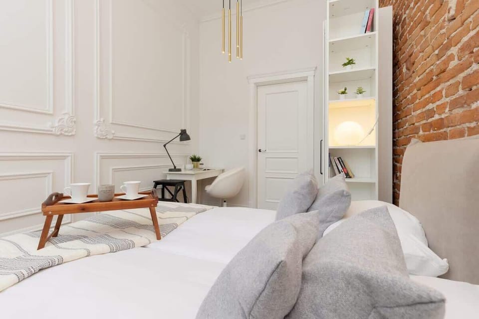 A mix of contemporary and rustic decor in a bedroom with a gray bed frame, brick wall, and clean white lines.