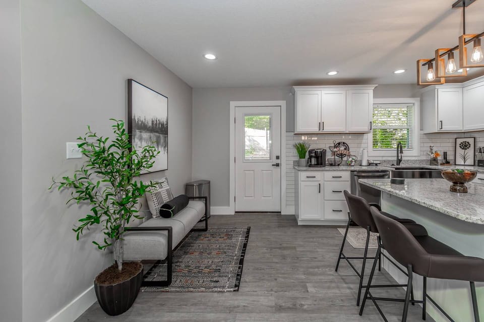 View looking into the kitchen area with island to the right, sitting bench to the left and back door leading to porch and yard straight ahead