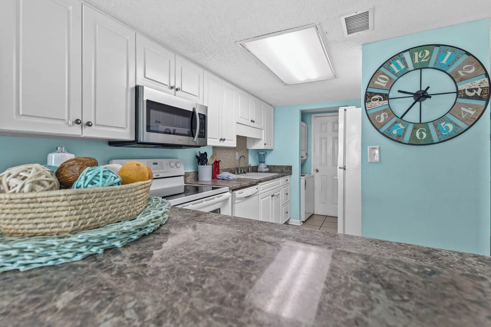 Bright kitchen featuring white and stainless appliances, granite countertops, and decorative coastal accents