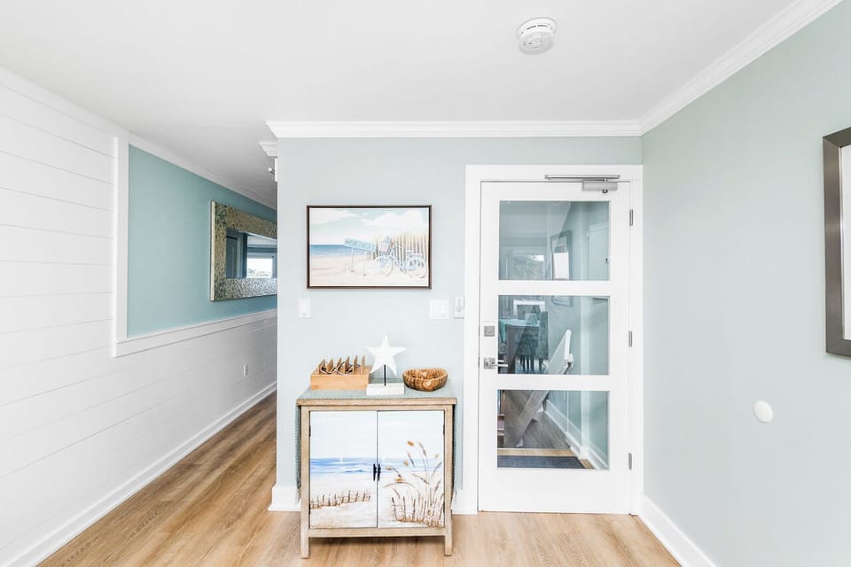 Step into your coastal retreat where soothing mint walls and warm hardwood create a serene atmosphere, complemented by charming beachside artwork.