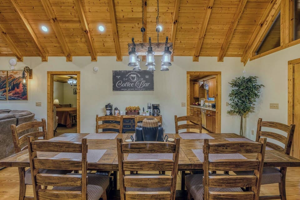 Nestled in a charming woodland setting, the dining area boasts a handcrafted 7-foot rectangular table, ideal for seating eight. Its warm wooden tones, paired with soft ambient lighting and earthy decor, create a welcoming space for memorable meals