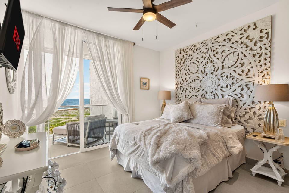 Ocean-view bedroom with a private balcony, Smart TV, AC, ceiling fan, and bedside outlets.
