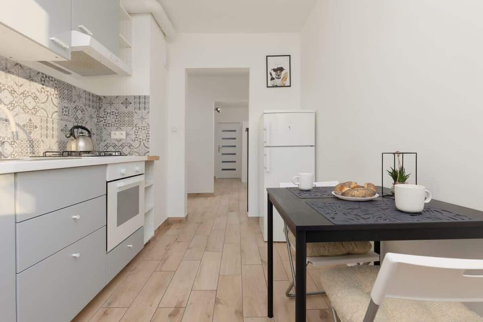 A wider view of the kitchen, showing a dining table with two chairs, modern appliances, and a bright atmosphere.
