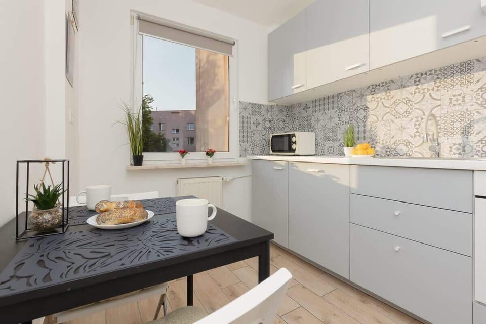 A modern kitchen with grey cabinets, a tiled backsplash, and decorative elements on the counter, all lit by natural light from a window.
