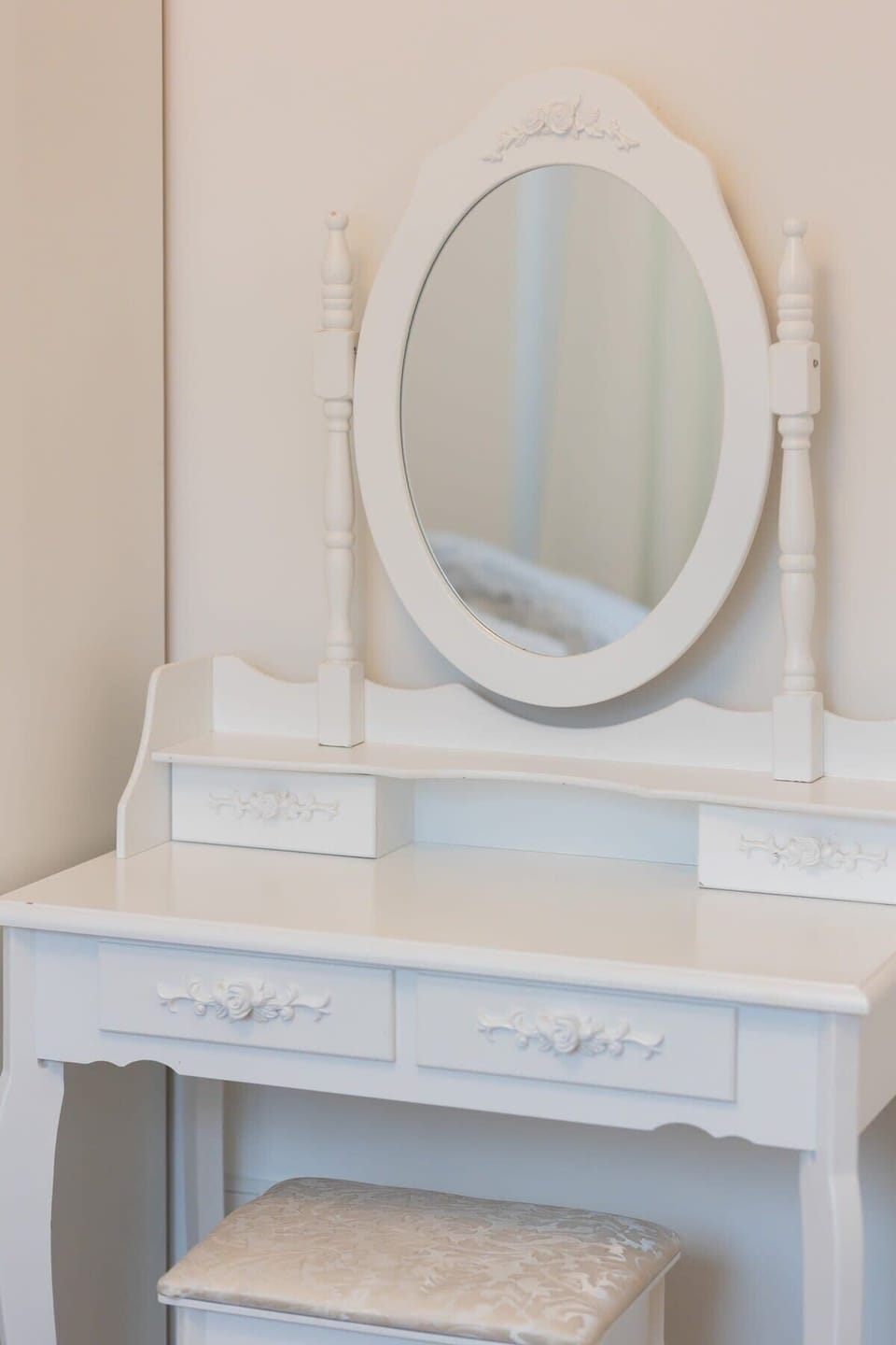 A close-up of the dressing table, complete with a stool and a round mirror in a bright bedroom.
