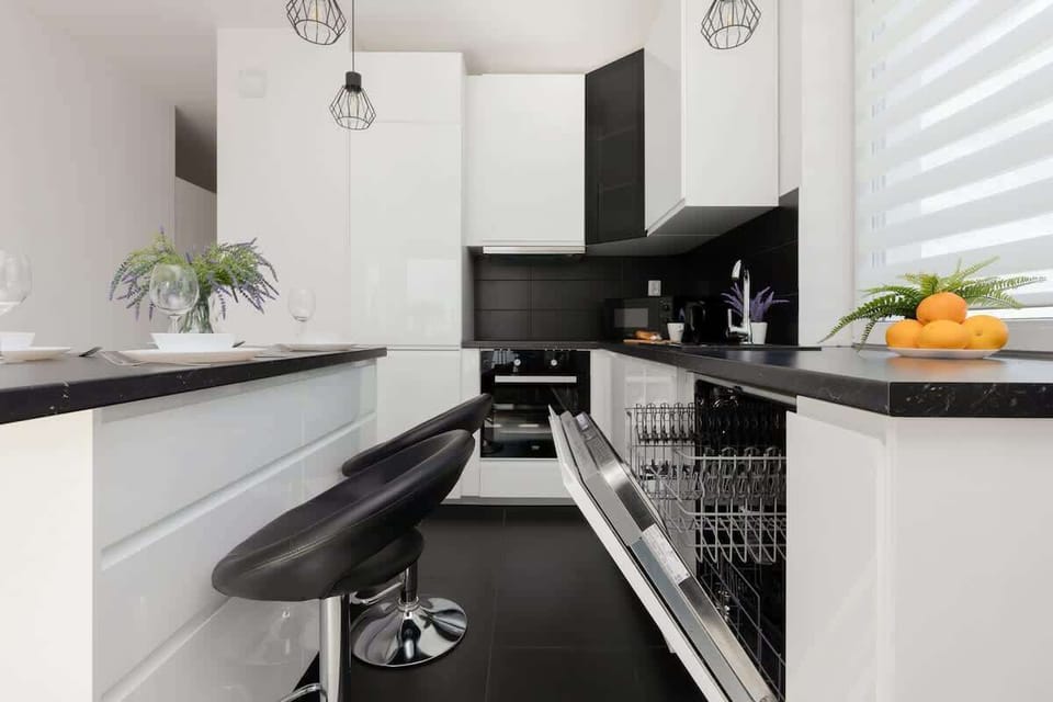 A modern kitchen with a black and white color scheme, featuring a breakfast bar with two stools and a bowl of fresh oranges as a decorative element.





