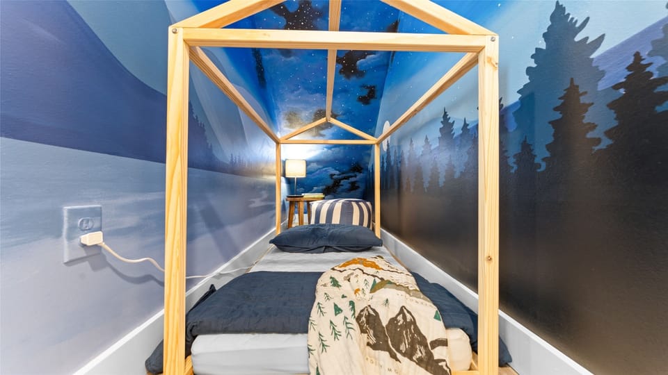 Kids’ glamping nook downstairs—house-frame bed under a starry mural.