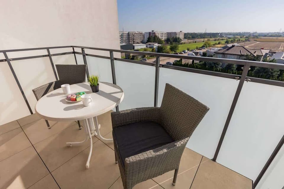 A cozy balcony with two wicker chairs, a small table, and a panoramic view of the surrounding cityscape.
