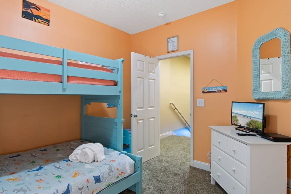 Your kids will love this cheerful bunk room with bright turquoise beds, fun beach decor, and their own TV for movie nights after beach adventures.