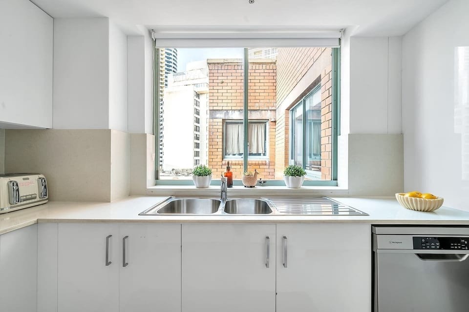 The kitchen features a large sunny window with beautiful city views and roller shades. The cabinetry is stocked with pots, pans, cutlery and crockery to ensure all you need is your favourite recipe ingredients. 