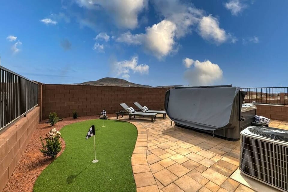 Large patio with putting green, hot tub, lounge chairs, and patio table. 