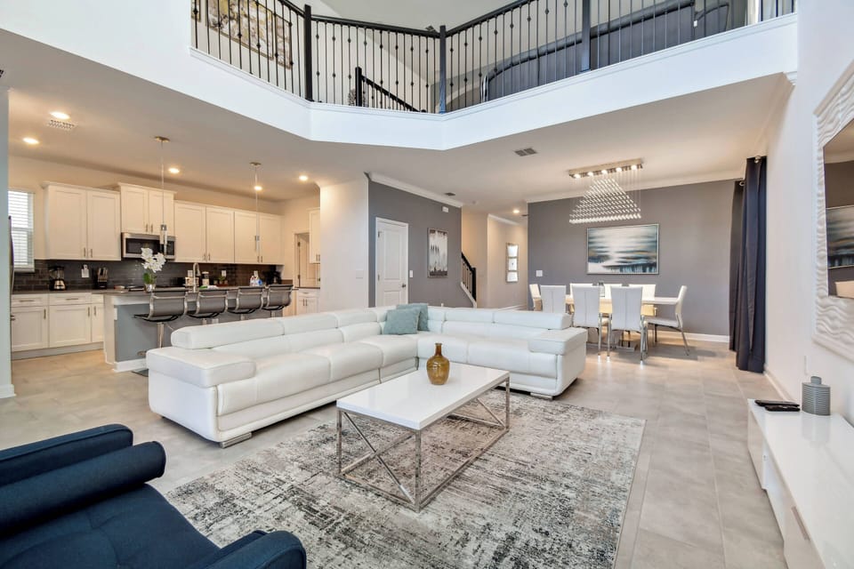 Enjoy the spacious living area filled with natural light from large windows, highlighting the sleek white sectional and modern decor. The open layout seamlessly flows into a chic dining space, ideal for gatherings.