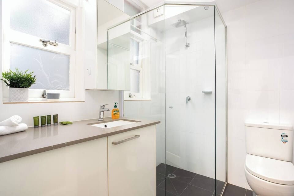 A pristine bathroom with a rainshower, spacious vanity and sleek black-tiled floors.