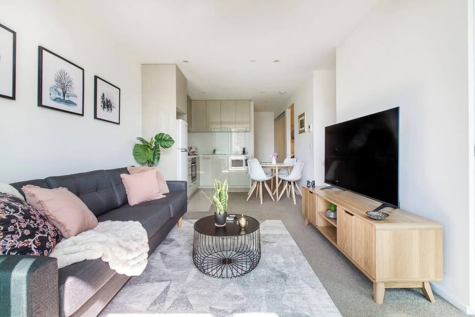 The living area features a large sofa and TV, with large windows maximising natural light and creating a sense of spaciousness. 
