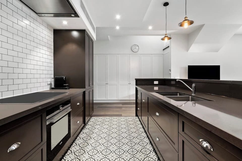 The monochrome theme continues on in the kitchen, featuring patterned tiles, dark timber cabinets and white subway tiles—plus all the essentials to whip up a meal at home.