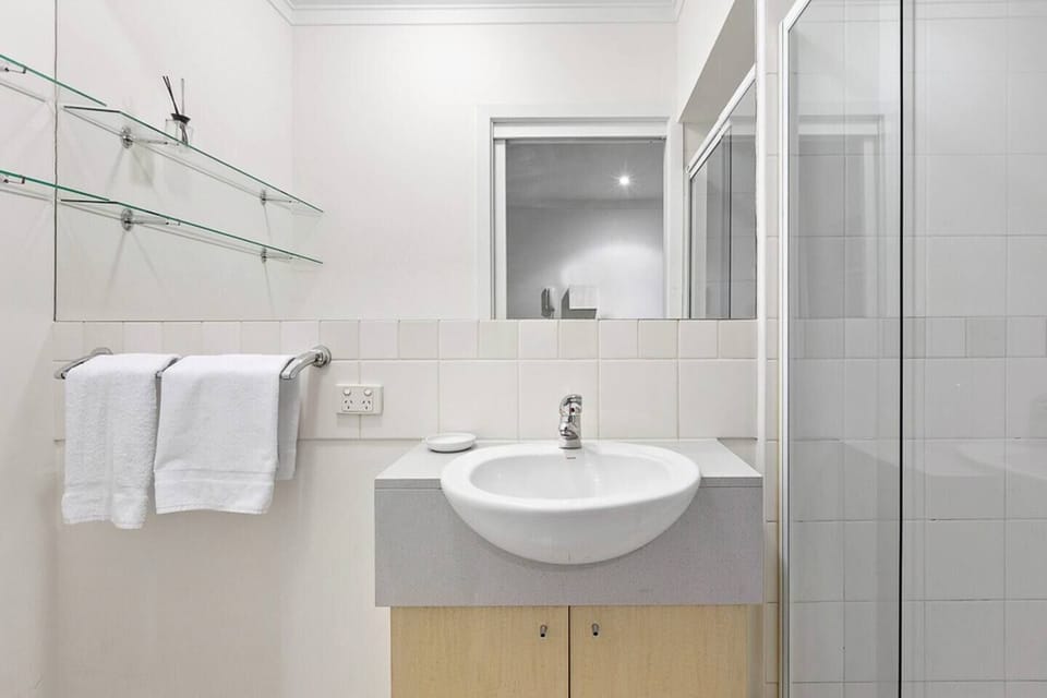 Freshen up in the compact bathroom featuring a vanity, wall-to-wall mirror, toilet and glass shower.