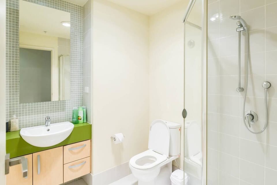 The bathroom features pops of colour with neutral tones. Wash up in the glass shower with adjustable head and get ready at the vanity with storage. 