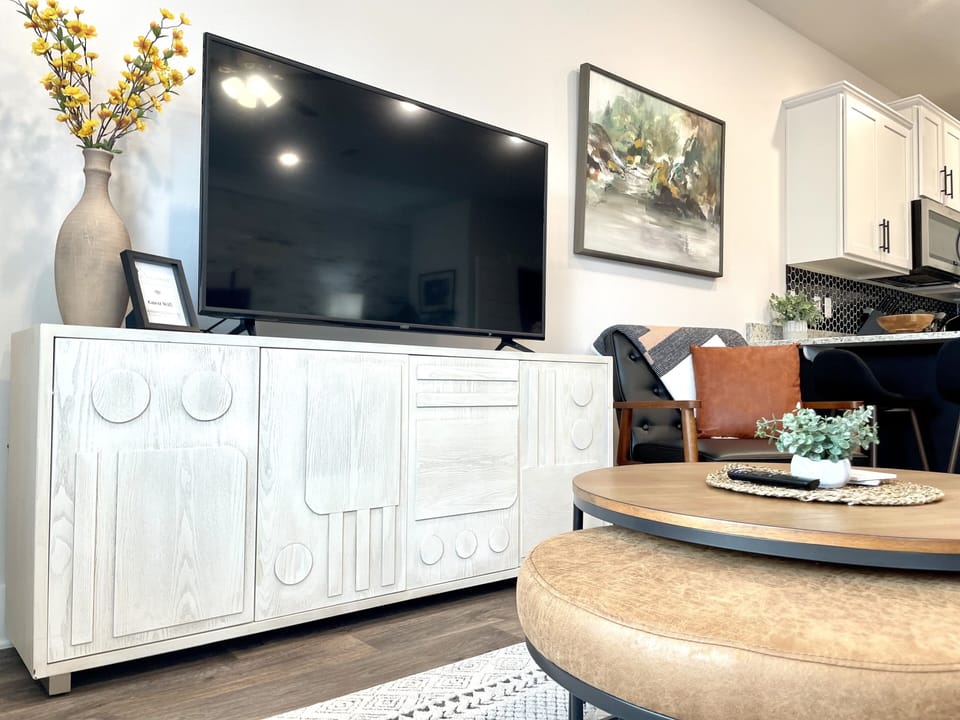 Living Room Bliss: Experience the Perfect Balance of Comfort and Entertainment in our Living Room, Featuring a Stunning 55-Inch TV as the Focal Point. Surrounding it, a Convenient Coffee Table, and a Plush Padded Ottoman Create the Ideal Setting for Relaxing, Socializing, and Enjoying Your Favorite Shows or Movies in Style.