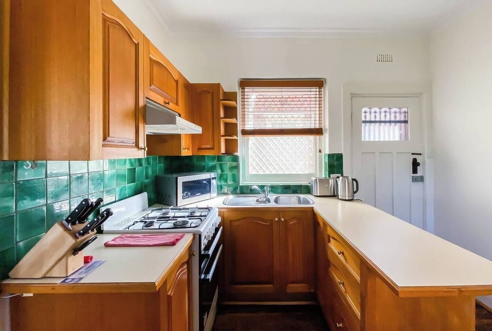 The kitchen is defined by teal tiling and timber cabinets, fully-equipped for those looking to cook at home.