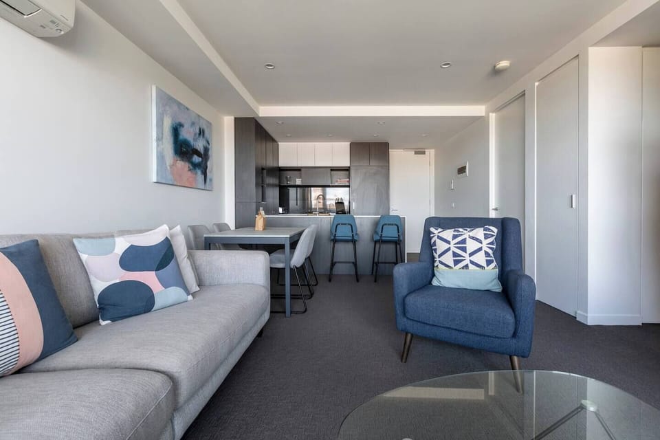 A lounge area that features a sleek, grey couch, comfortable armchair, sleek glass-topped coffee table and a wide-screen, LCD TV that is mounted onto the wall and offers both Netflix and Foxtel