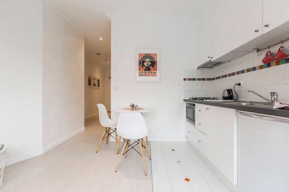 A compact kitchen is equipped with a two-person dining table, dishes and cutlery, small fridge, microwave, gas stovetop and wine glasses