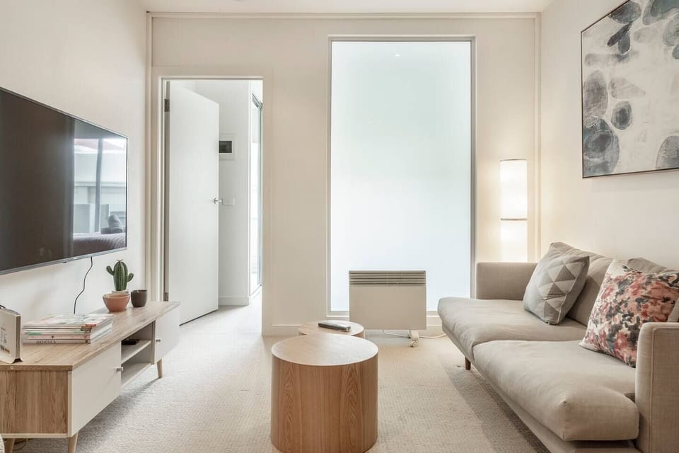 A comfortable living area features a sleek, two-person couch, modern timber furniture and a wide-screen LCD TV