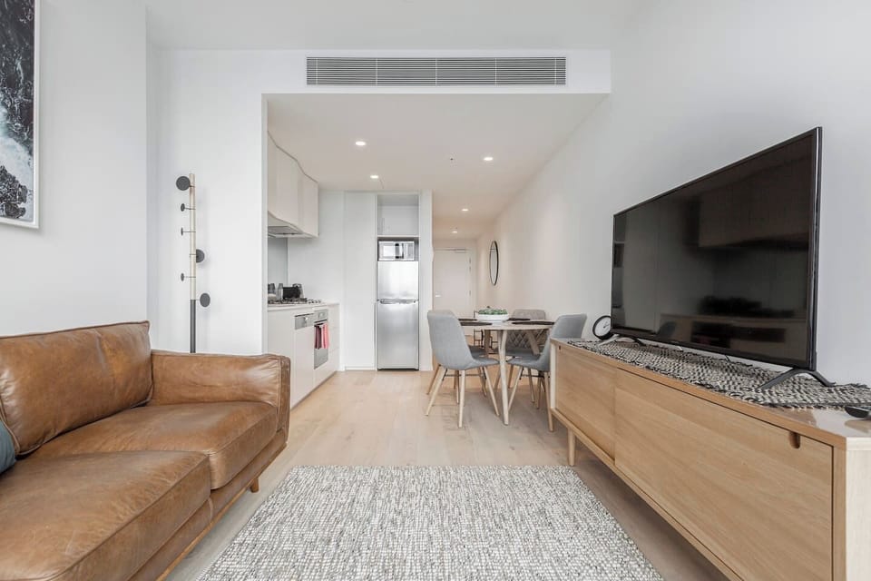 A beautifully-designed living room comes furnished with a large, flat-screen smart TV and a plush brown leather couch