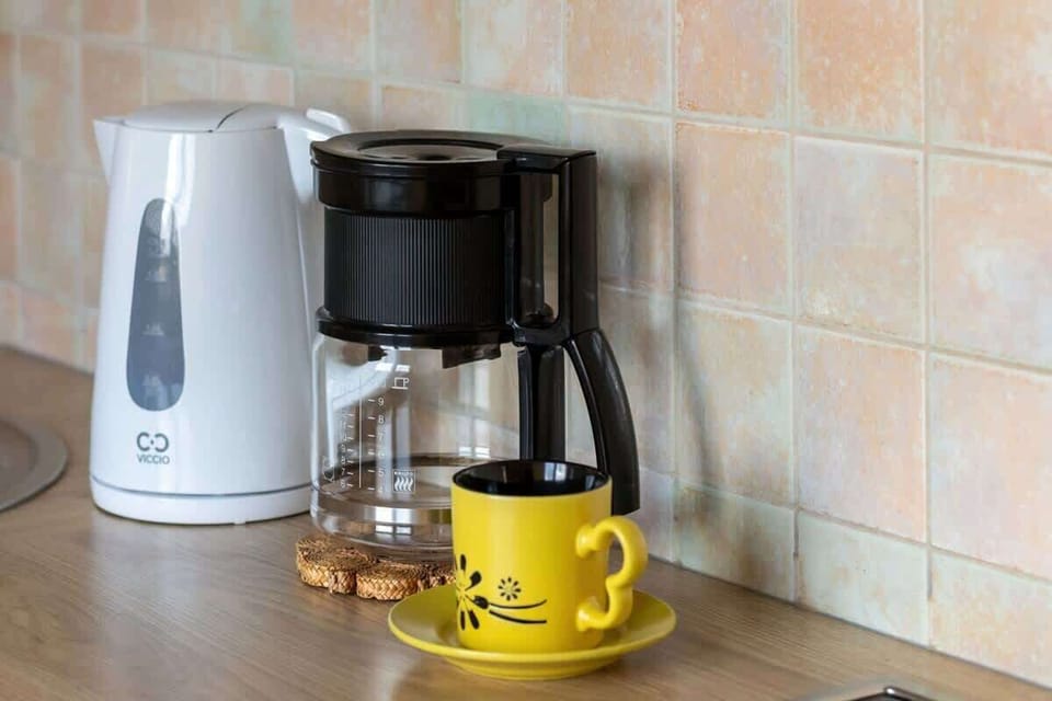 A close-up of a coffee station with a white coffee maker, yellow mug, and tiled backsplash, perfect for morning routines.






