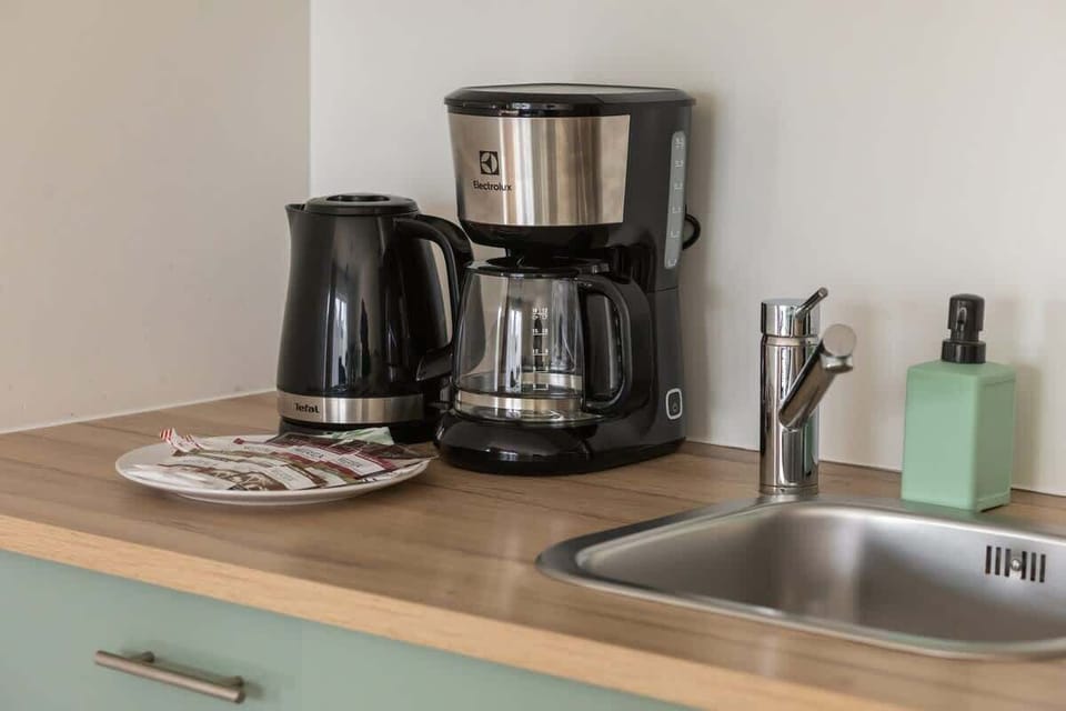 A kitchen corner with a coffee maker, kettle, and mint green cabinets.

