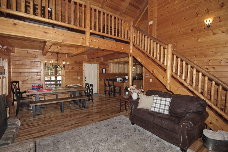 Beautifully crafted cabin interior featuring a lofted second level, rustic wood staircase, and spacious dining area—perfect for family meals and game nights.