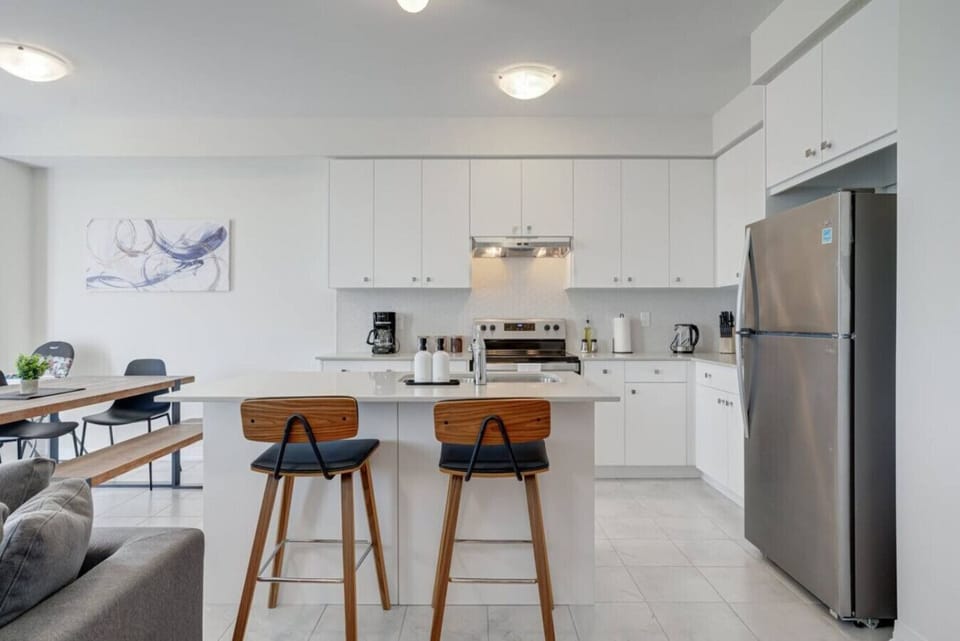 Cook, dine, and connect in this bright, modern kitchen featuring sleek white cabinetry, stainless steel appliances, and a spacious island with seating for two. Whether you are brewing a fresh cup of coffee in the morning, preparing a family meal, or shari