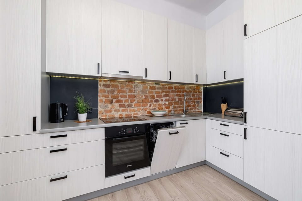 A modern kitchen featuring white cabinets, a brick backsplash, and built-in appliances for a stylish and functional design.
