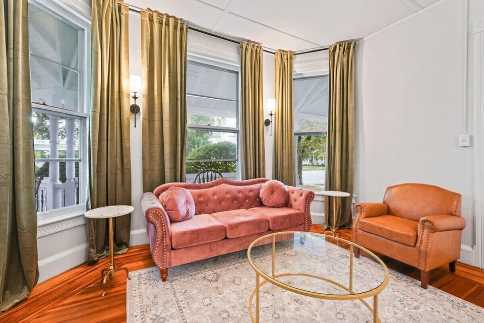 Living Room with Rose Couch, Arm Chair, Stylish Sconce LIghts and Floor to Ceiling Privacy Window Treatments