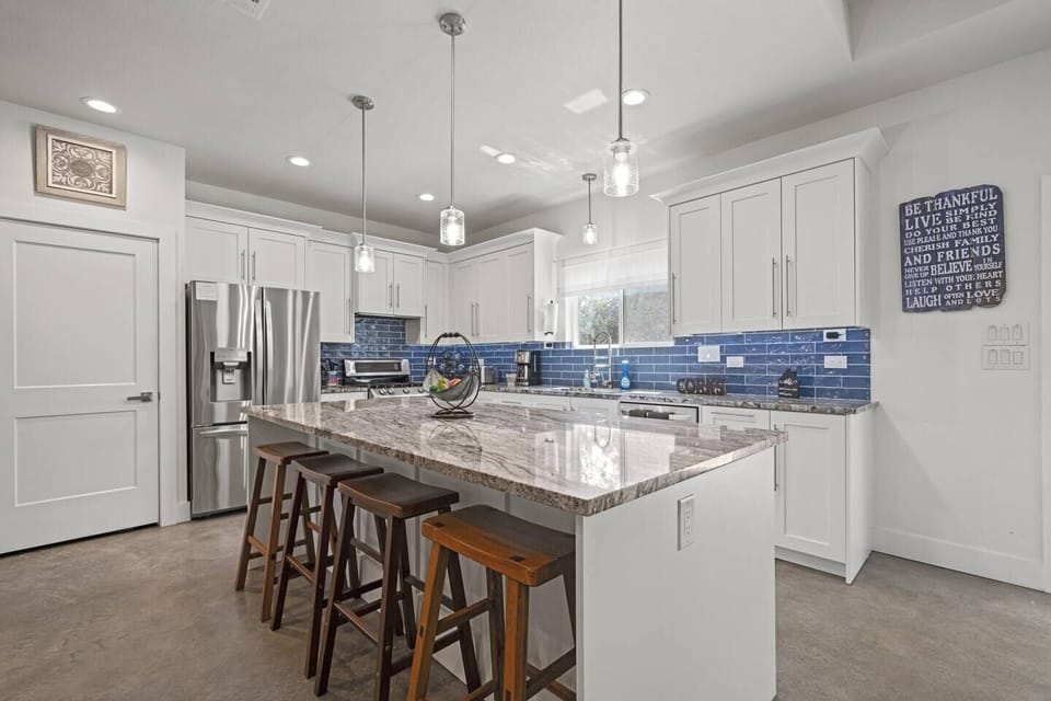 Spacious kitchen with an island, stainless steel appliances, and a vibrant blue backsplash.