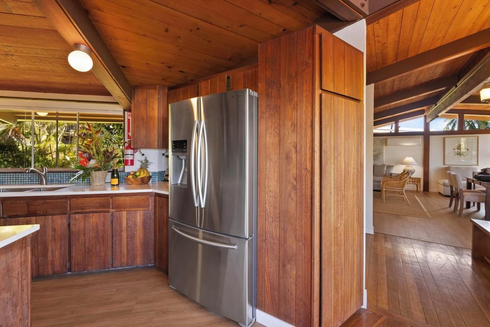 Spacious kitchen with stainless steel appliances, rich wood cabinets, and a scenic garden view, perfect for a Hawaiian culinary retreat.