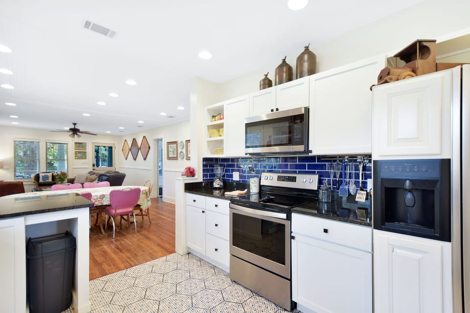 Open Kitchen With Navy Tile Backsplash - White cabinets, stainless appliances, and the navy backsplash sit beside the dining area for easy meals after East Beach.