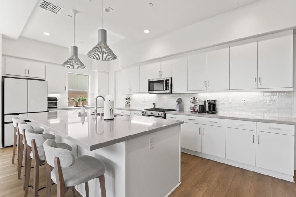 Sleek white kitchen w/ large island seating, modern finishes & pendant lighting.