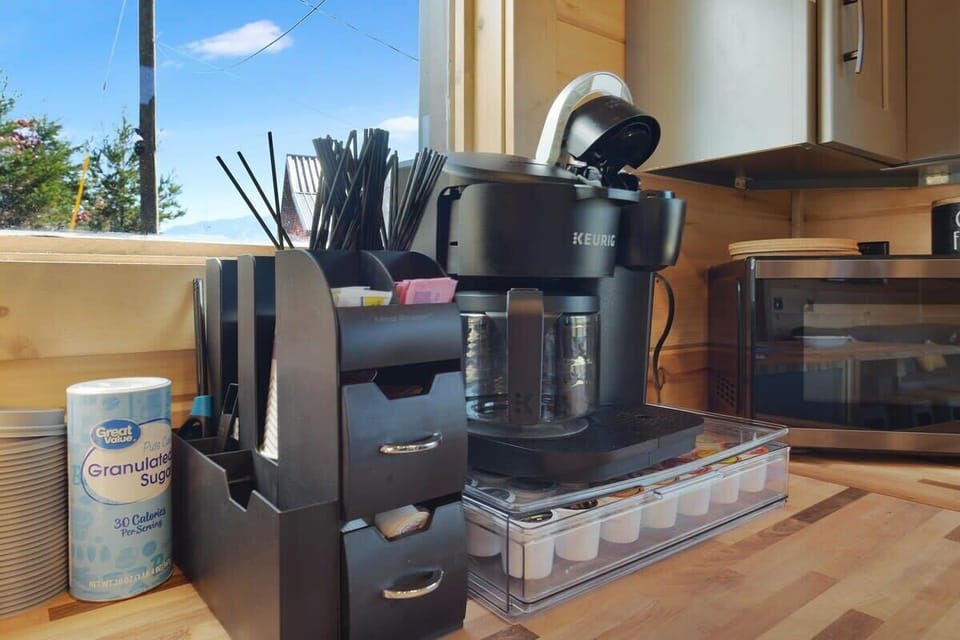Modern coffee station with a keurig machine and organized supplies by a window.